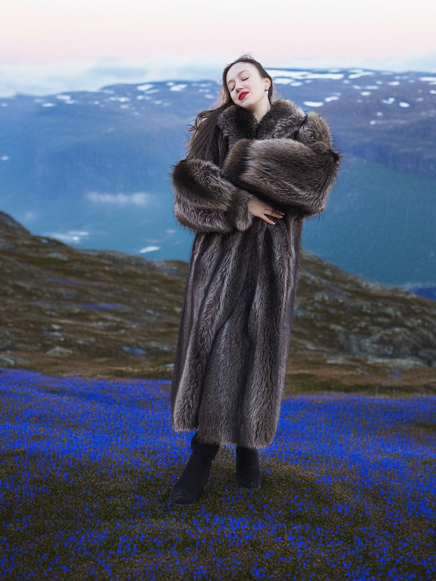 Real fur raccoon coat in silver tips, full-length and warm, modeled in alpine field with blue flowers, luxury winter apparel.