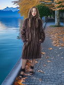 Woman in a fur coat standing by a lake with mountains in the background