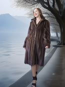 Woman in a fur coat standing by a lake with mountains in the background