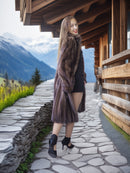 Woman in a fur coat standing on a stone path with mountains in the background