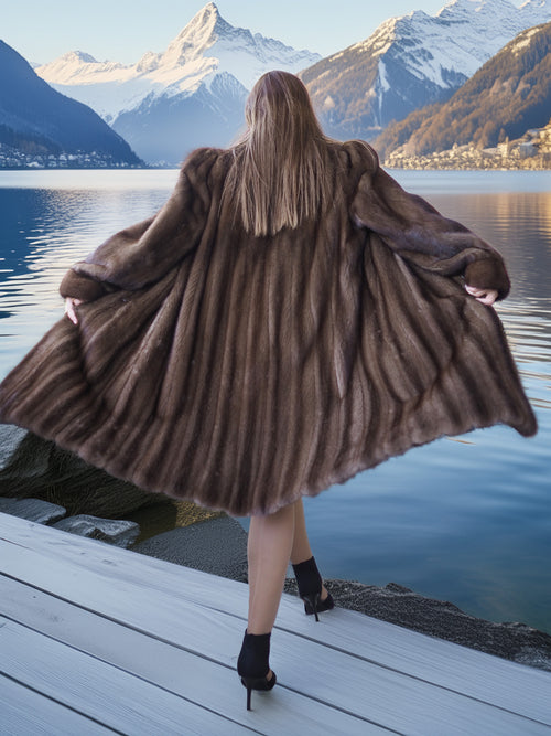 Person wearing a fur coat standing on a dock with mountains and lake in the background