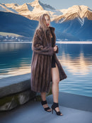 Woman in a fur coat standing by a lake with mountains in the background
