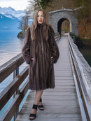Woman in a fur coat standing on a wooden bridge over a lake with mountains in the background