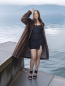 Woman in a long brown coat standing on a dock by water