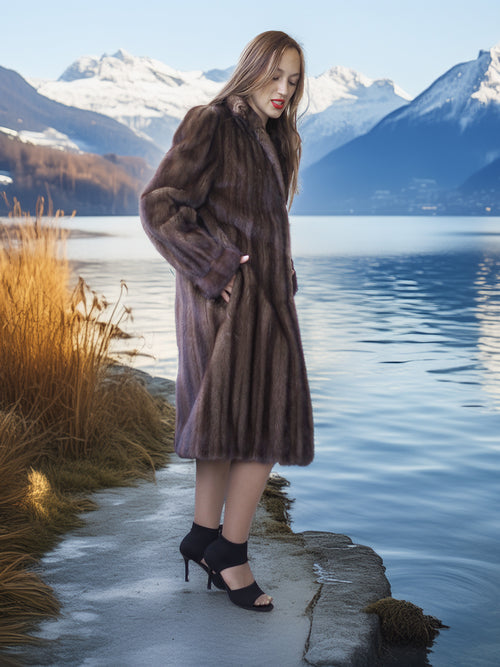Woman in a fur coat standing by a lake with mountains in the background