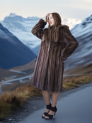 Woman in a fur coat standing on a mountain road with snow-capped mountains in the background