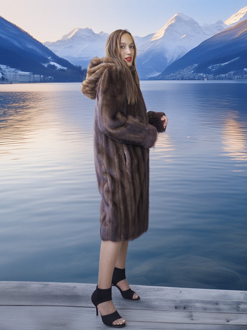 Woman in a fur coat standing by a lake with mountains in the background