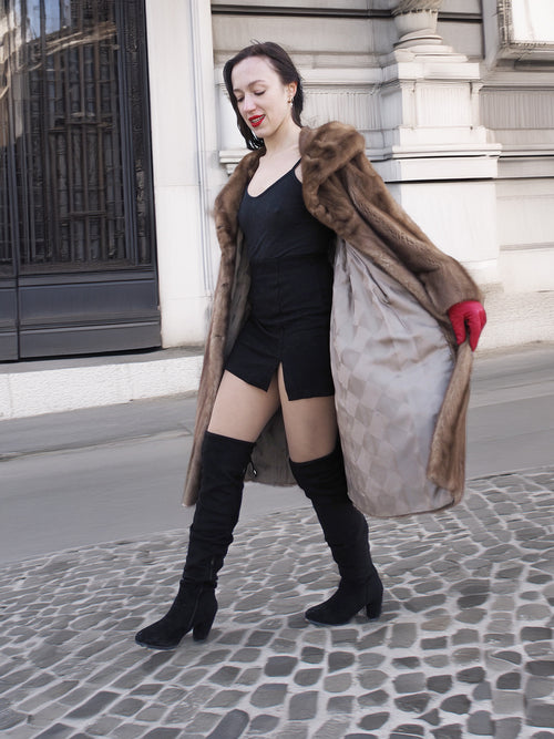 Vintage pastel Canadian brown mink fur coat open to reveal satin lining, styled with black dress and boots for modern winter elegance.