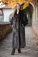 Woman wearing a long fur coat standing on a cobblestone path with autumn leaves.