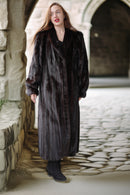 Woman wearing a long dark coat standing in front of stone walls and a door.