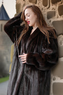 Woman wearing a dark fur coat against a stone wall.