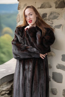 Woman wearing a fur coat standing against a stone wall with a scenic background