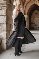 Woman in a long black coat standing in front of stone arches