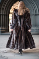 Person wearing a long fur coat walking away in an indoor setting with architectural elements.