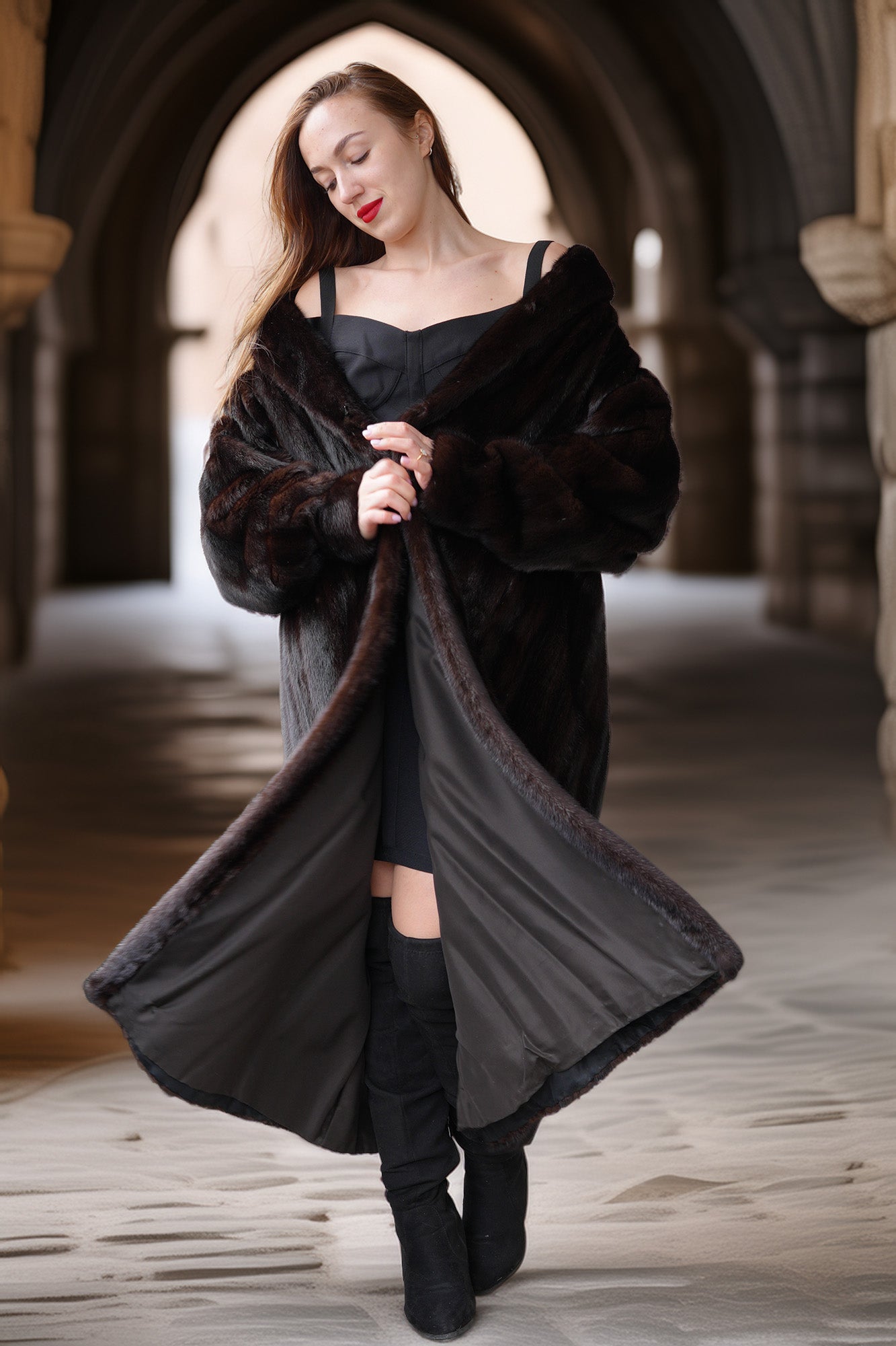 Woman wearing a long black coat with fur trim in an archway.