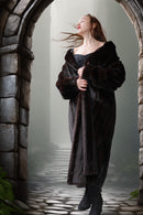 Woman in a long dark fur coat standing in a stone archway with a foggy background
