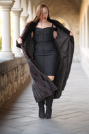 Woman in a black dress holding a black coat in an outdoor setting with columns.