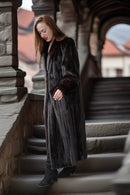 Woman in a long dark coat standing on stone steps with architectural background