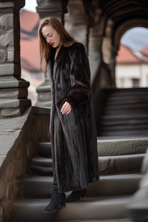 Woman in a long dark coat standing on stone steps with architectural background