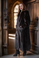 Woman in a long dark coat standing in front of a wooden door with stained glass.