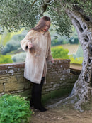 Woman in a beige coat standing next to an olive tree with a scenic background