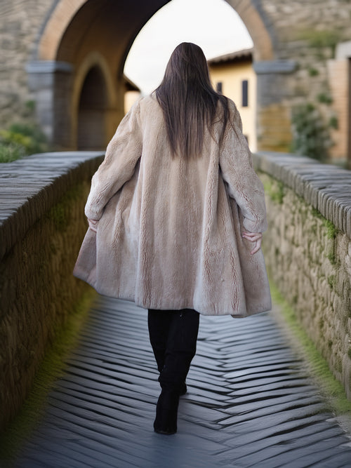 Person wearing a long coat walking on a stone bridge with a stone building in the background