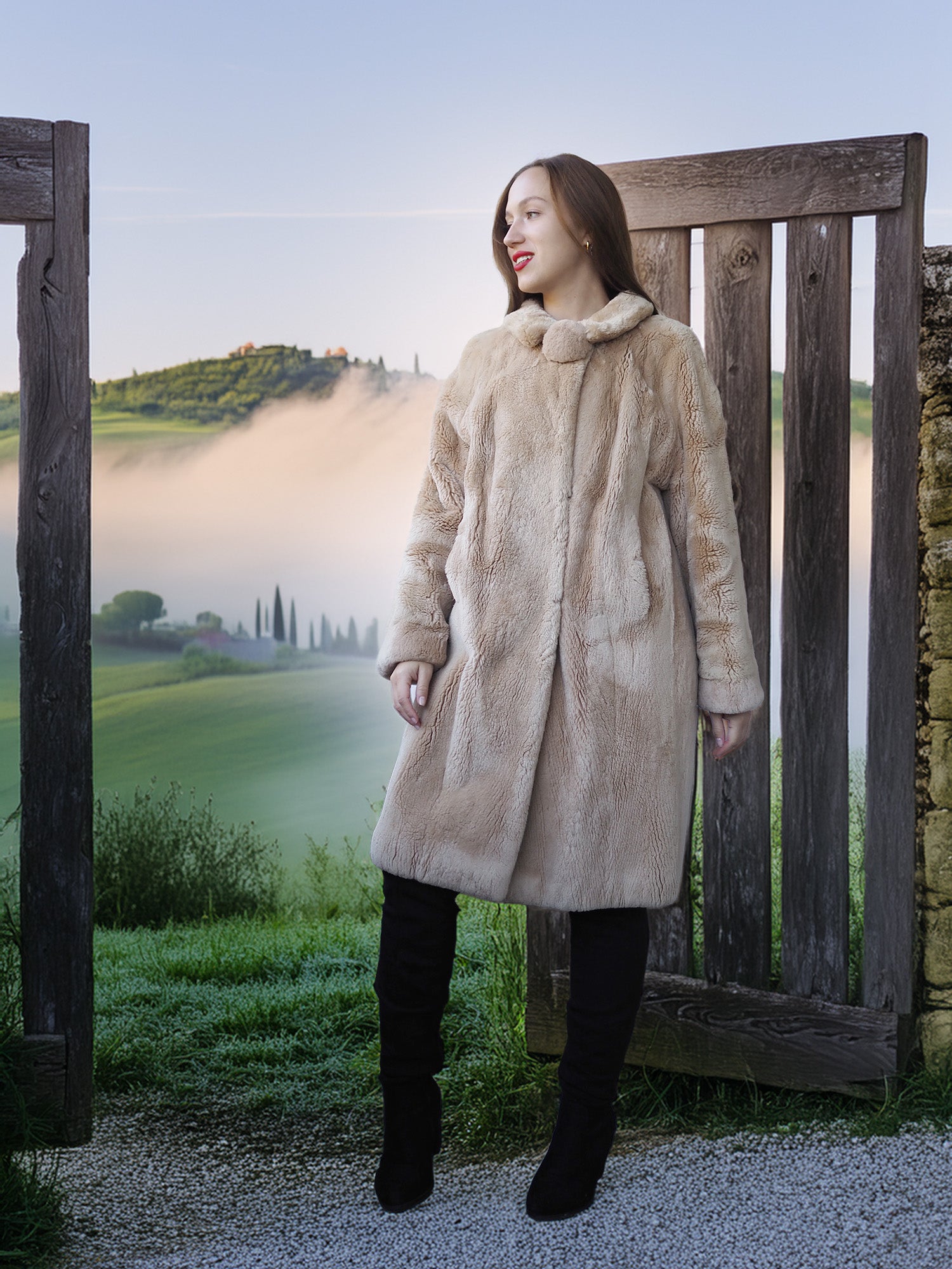 Woman in a fur coat standing in a scenic outdoor setting with a wooden gate and misty landscape.
