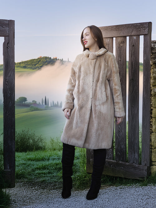 Woman in a fur coat standing in a scenic outdoor setting with a wooden gate and misty landscape.