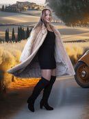 Woman in a fur coat and black dress standing in a scenic outdoor setting with a vintage car.