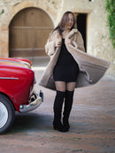 Woman in a long coat and knee-high boots standing next to a vintage red car.