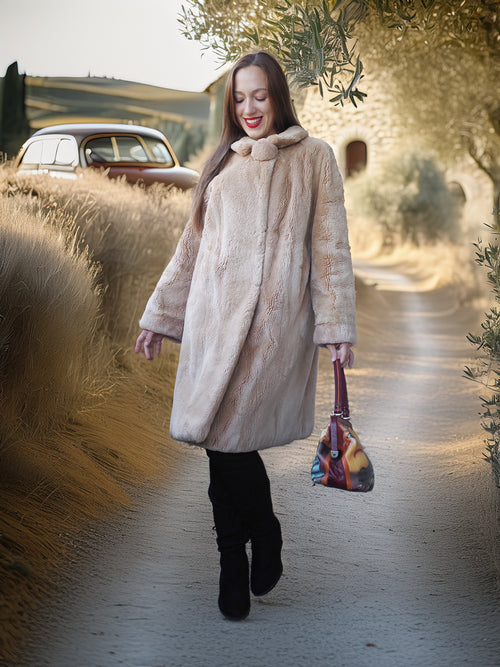 Woman in a long beige coat walking outdoors with a vintage car and trees in the background