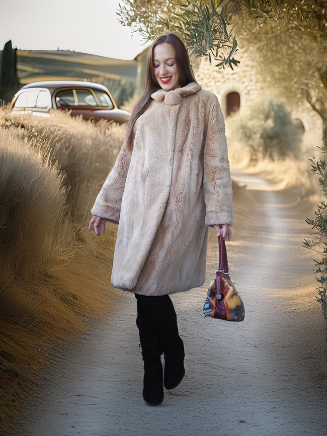 Woman in a long beige coat walking outdoors with a vintage car and trees in the background