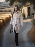 Woman in a long beige coat walking on a path with a scenic background