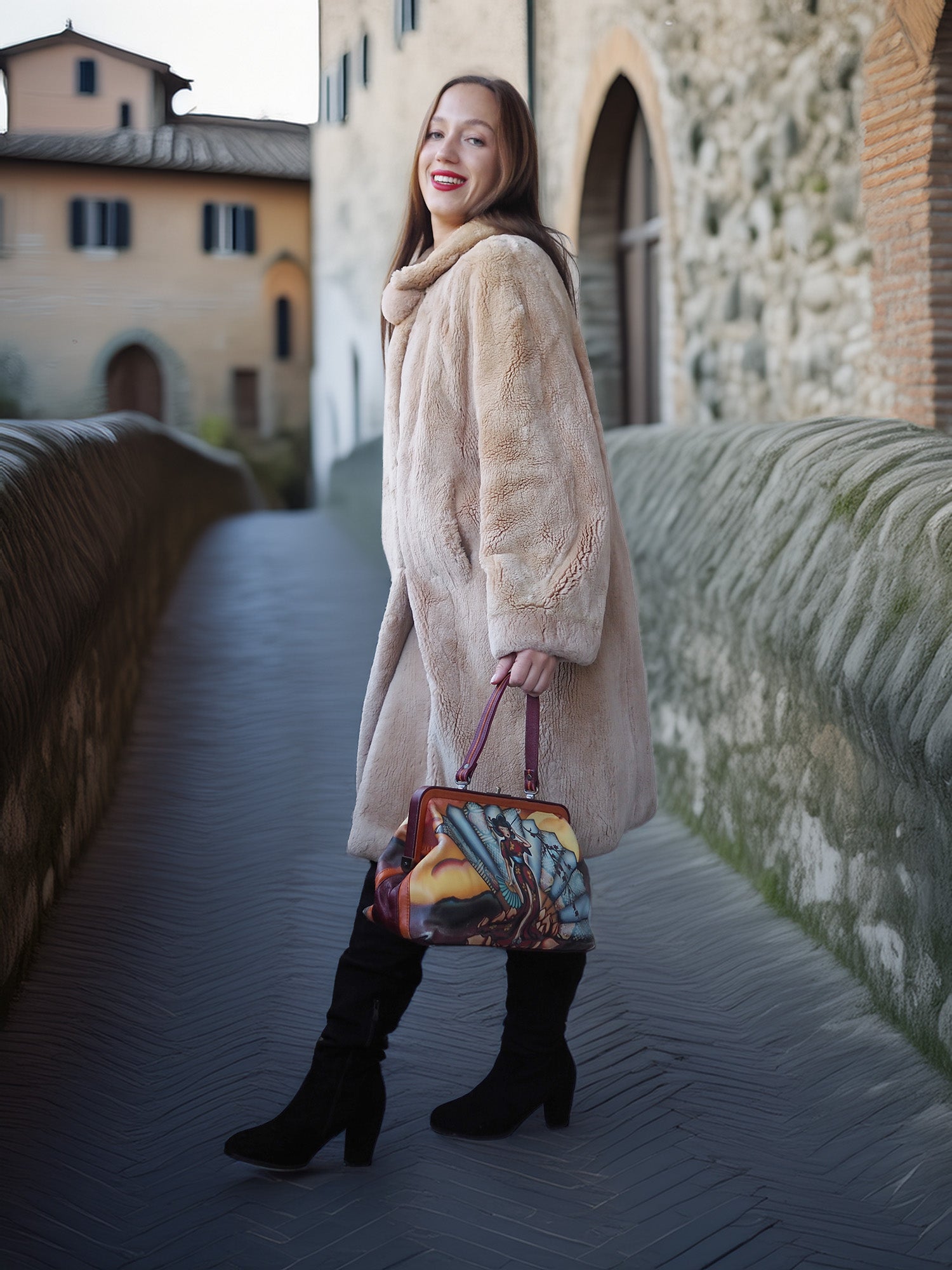 Woman in a beige coat holding a colorful handbag on a stone bridge.