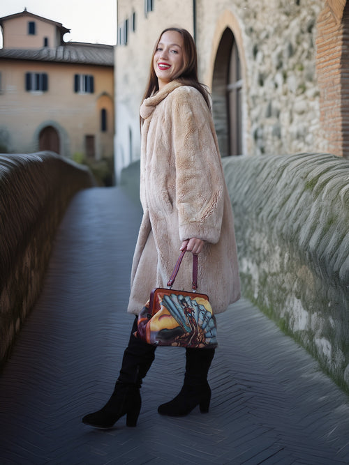 Woman in a beige coat holding a colorful handbag on a stone bridge.