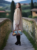 Woman in a fur coat holding a colorful handbag on a stone path with a scenic background