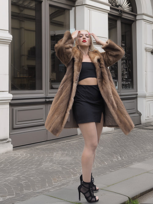 Classic pastel brown mink fur coat stroller jacket M/L styled with black mini dress and heels in urban setting. Luxurious natural fur outerwear.