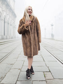 Smiling model in classic pastel brown mink fur coat stroller jacket M/L on foggy tramway. Luxurious and timeless fur fashion piece.