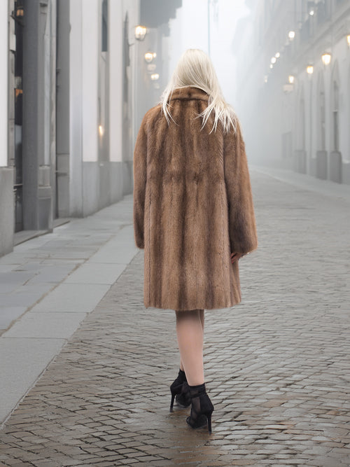 Back view of classic pastel brown mink fur coat stroller jacket M/L walking down cobbled street. Elegant and soft natural mink fur.