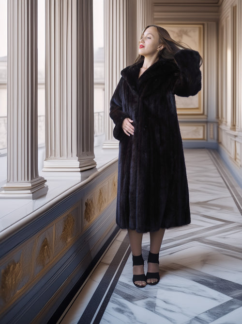 Woman in a black fur coat standing in an elegant interior setting with columns and marble floor.