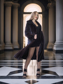 Woman in a long dark coat standing in a classical architectural setting with columns and marble floor.