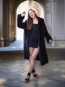 Woman in a long black coat standing in an elegant interior setting