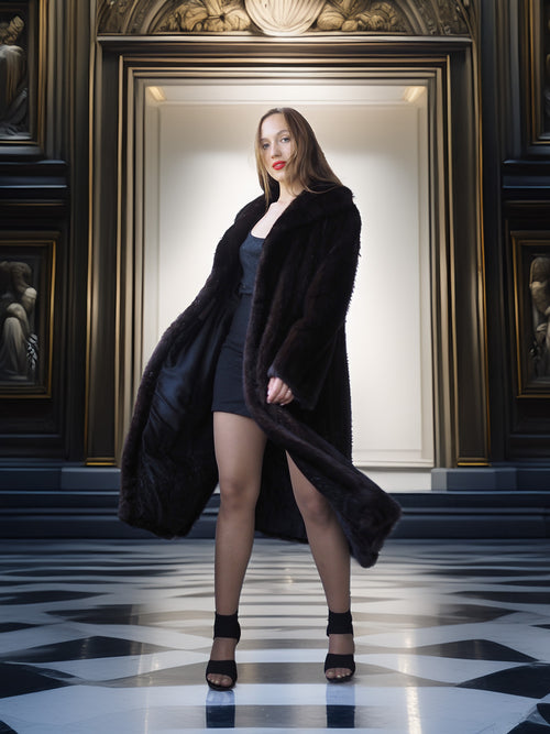 Woman in a long black coat standing in a room with classical decor