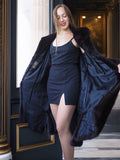 Woman wearing a dark blue dress with a fur-trimmed coat in an elegant interior setting.