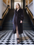 Woman in a long dark coat standing in an elegant interior setting with checkered floor and gold accents.