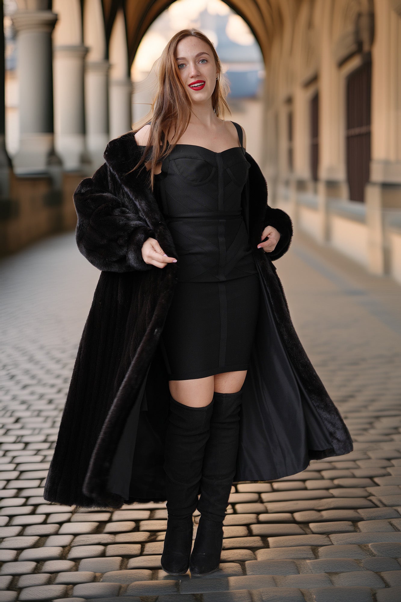 Woman in a black coat and dress standing on a cobblestone street.