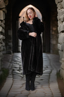 Woman wearing a black fur coat standing in a stone archway.