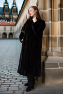 Woman in a black coat standing in front of a stone building with a cobblestone street.