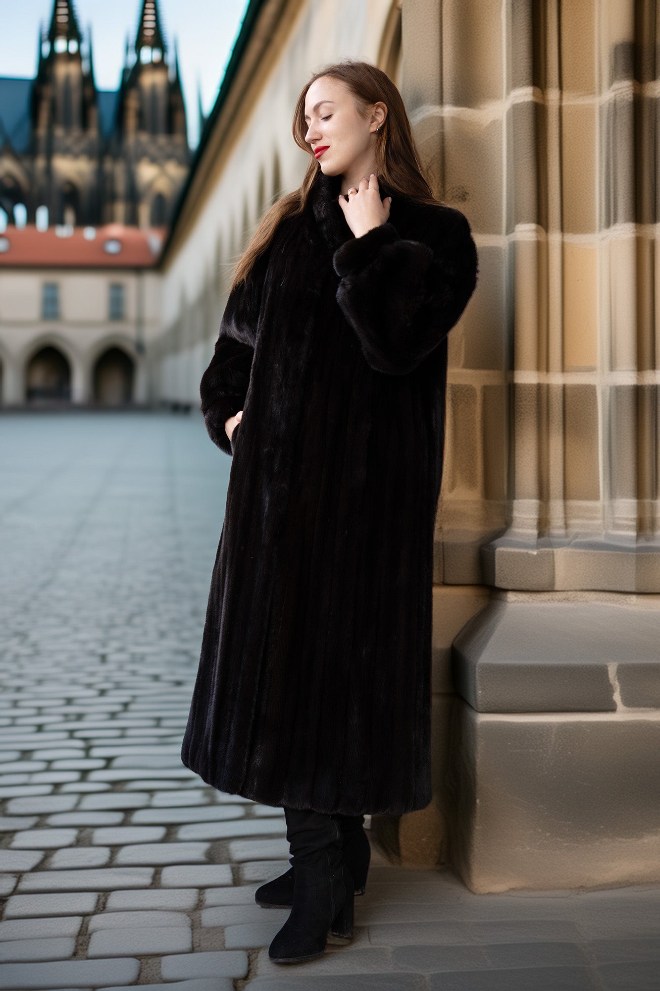Woman in a black coat standing in front of a stone building with a cobblestone street.