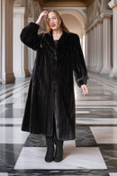 Woman wearing a long black coat in an elegant hallway with columns.